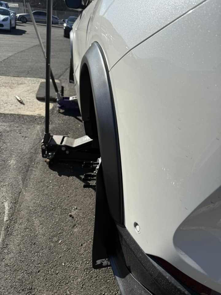 Close-up of a white car fitted with wider fender flares for enhanced tire clearance and aggressive stance