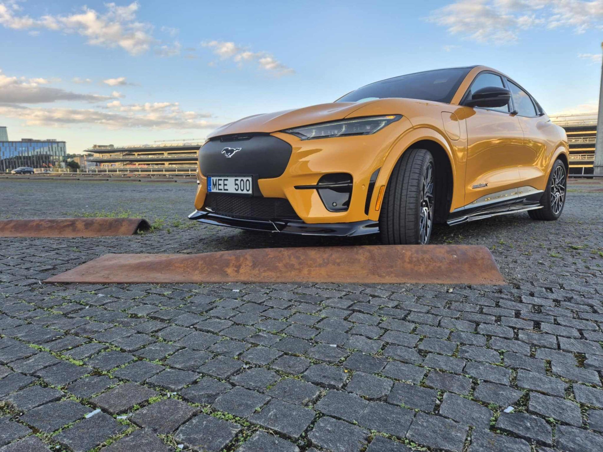 Yellow Mustang Mach-E GT with black front lip splitter installed on cobblestone surface