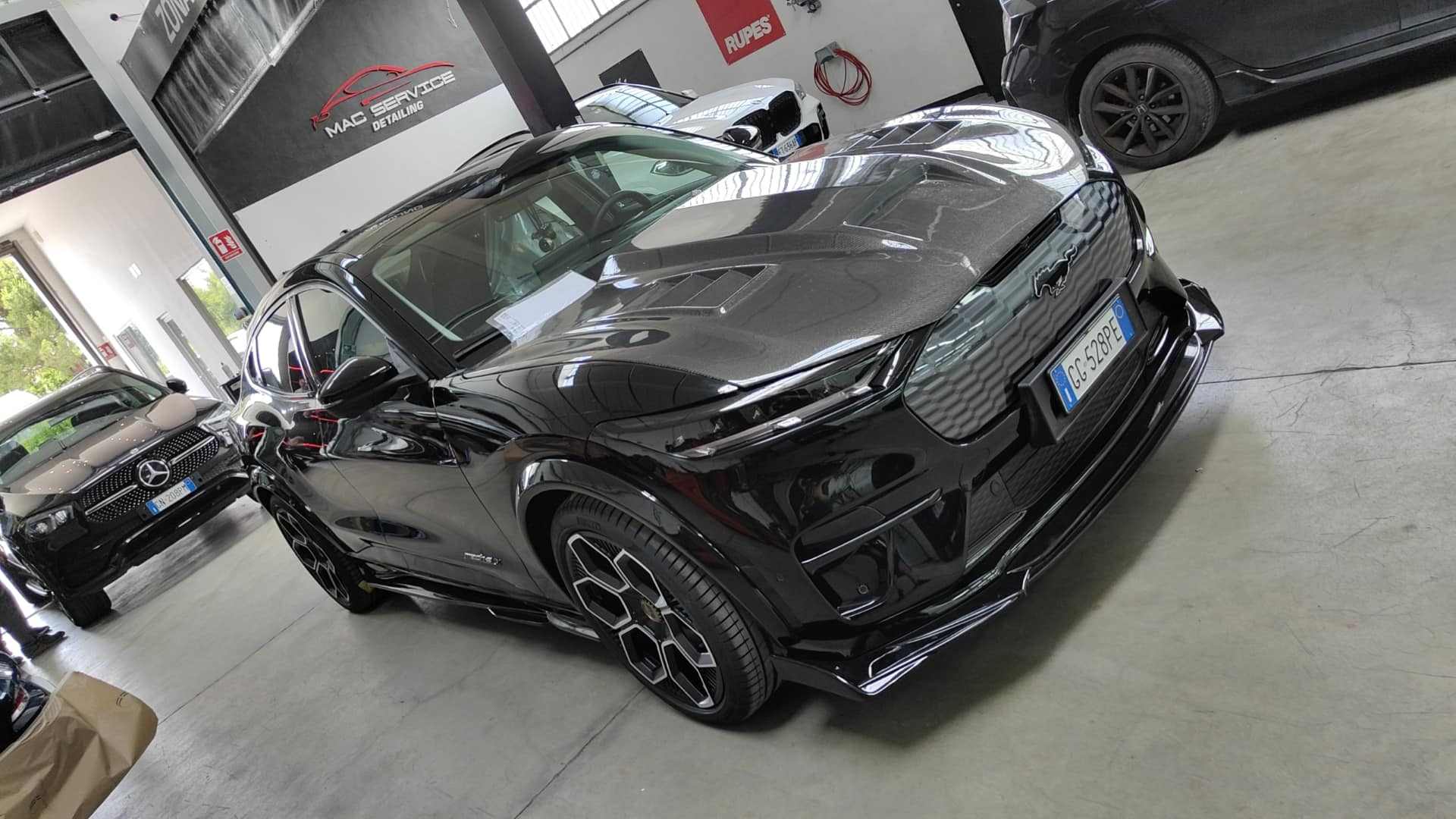 Black Ford Mustang Mach-E with Shelby GT550 style fiber hood upgrade in a garage