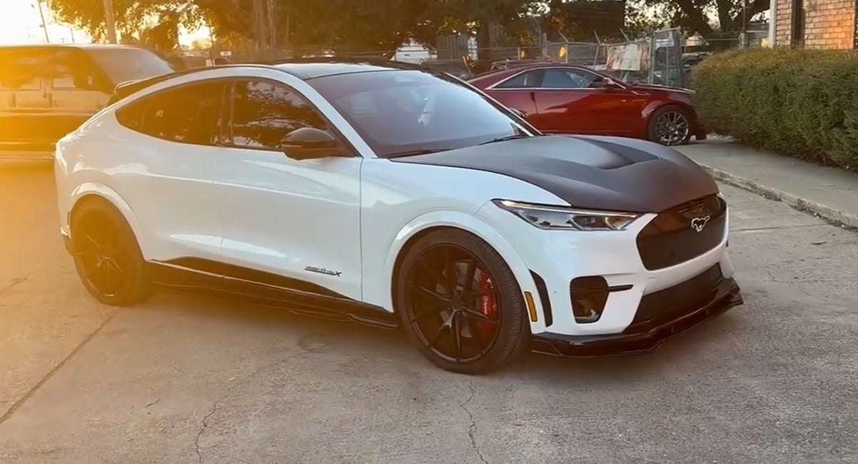 White Ford Mustang Mach-E with sleek black Shelby Style Fiber Hood parked outdoors at sunset