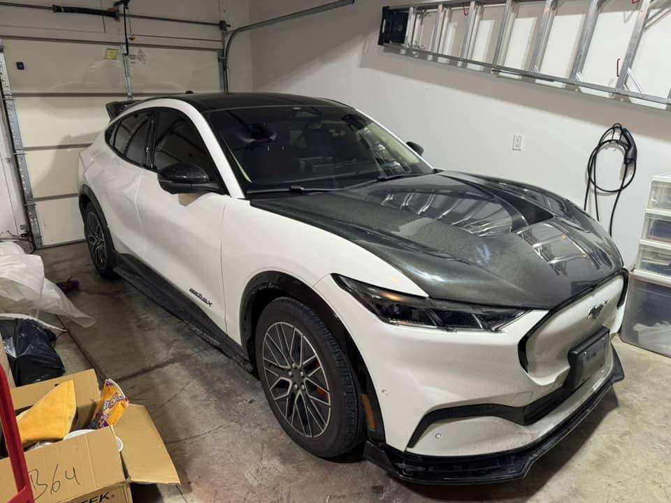 Ford Mustang Mach-E with Shelby Style Fiber Hood in carbon fiber finish parked in garage.