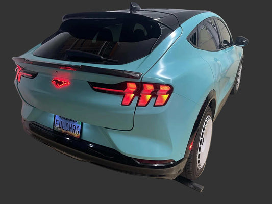 Rear view of a blue Mustang Mach-E with illuminated Light-Up Ponies emblem glowing red on the back.