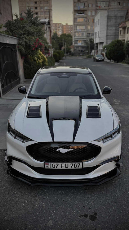 Front view of white Mustang Mach-E with Shelby GT550 style fiber hood featuring vents parked on city street