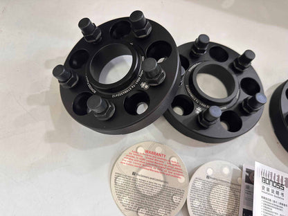 Black forged aluminum wheel spacers with extended wheel bolts on a white surface